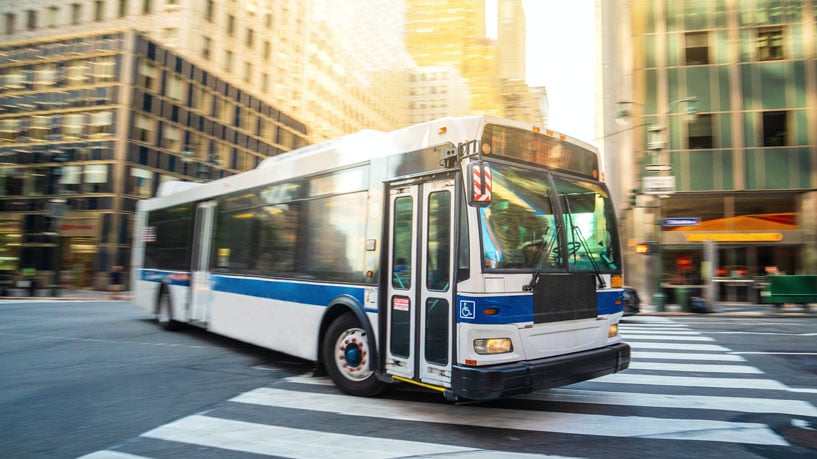 A city bus makes a left-hand turn, moving through a marked pedestrian crossing.